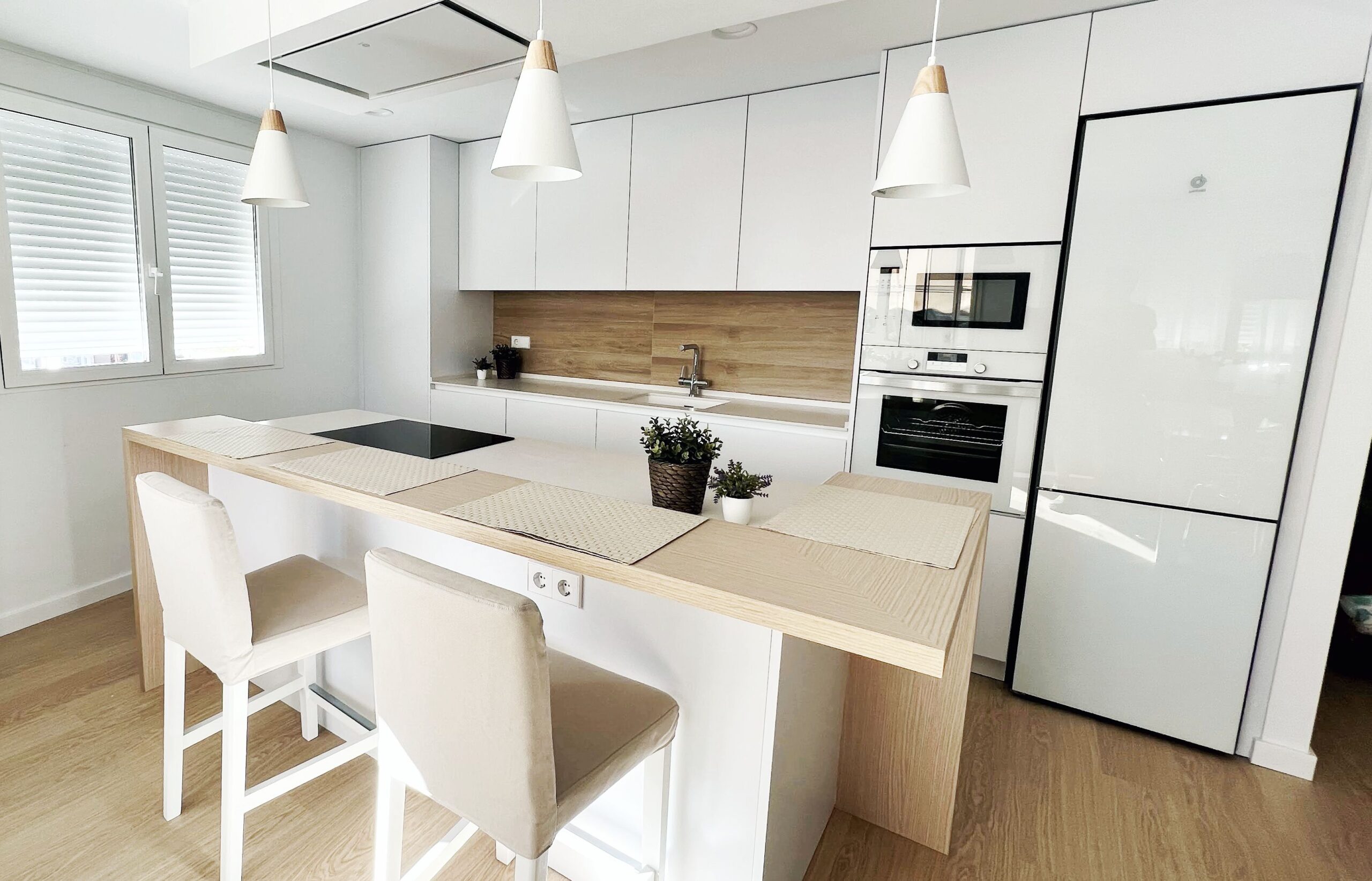 Reforma integral de cocina abierta con isla central en tonalidades blancas y madera en Valencia